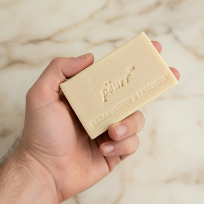 Cedarwood & Patchouli soap held in a man’s hand against warm marble