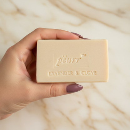 Lavender & Clove soap held by a woman with long berry-plum nails against warm marble