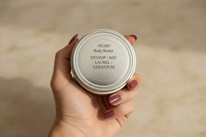 PËURR® body butter held with long muted berry-plum painted nails
