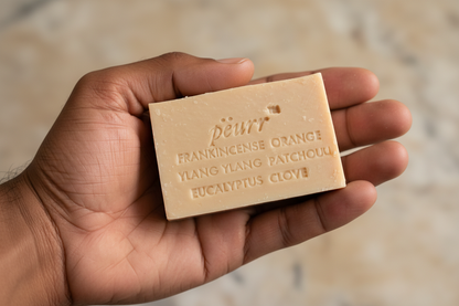 PËURR® Frankincense & Exotic Spice soap held in a man of color’s hand against warm marble