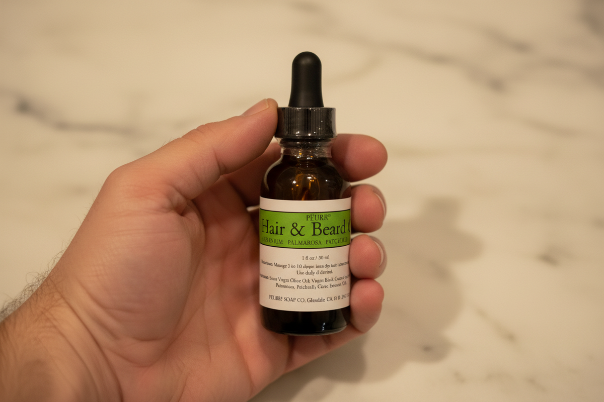 PËURR® Green Label Hair & Beard Oil held in a man’s hand against warm marble