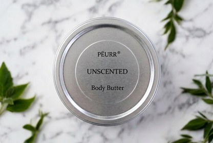 PËURR® Unscented Body Butter silver tin on white marble with green leaves.