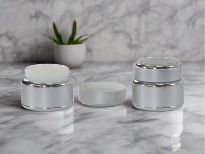 showing two jars of peurr body butter, one open and small plant in background against marble background