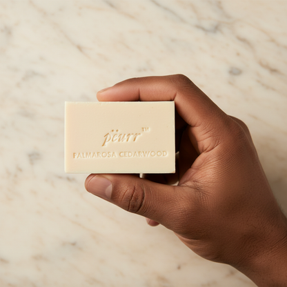 Palmarosa & Cedarwood soap held in a man of color’s hand against warm marble