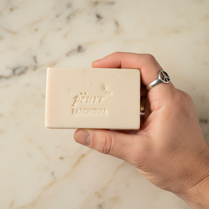 Patchouli soap held in a man’s hand wearing a silver peace-sign ring