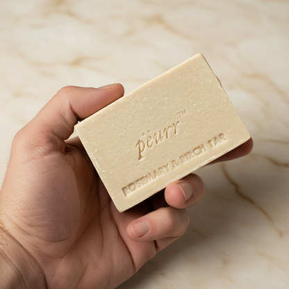 Rosemary & Birch Tar soap held in a man’s hand against warm marble