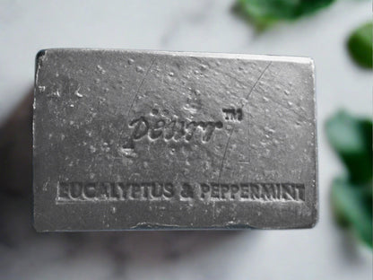 A bar of soap with 'PÈURR Eucalyptus & Peppermint' engraved on it, with a textured, gray surface.
