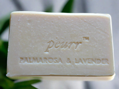 A bar of soap with 'Pëurr PALMAROSA & LAVENDER' embossed on it, placed against a floral patterned background.