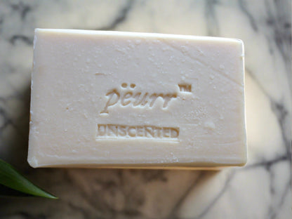 A bar of unscented goat milk and olive oil soap with the brand 'PëURR®' embossed on the top.