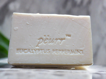 A bar of soap with 'PÈURR EUCALYPTUS PEPPERMINT' embossed on the top. The soap is white and the background is marble.