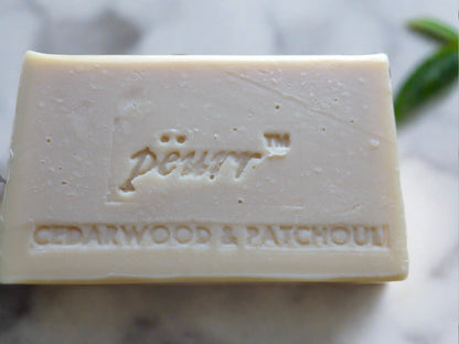 A bar of soap with 'pëurr Cedarwood & Patchouli' stamped into the top. The background is marble.