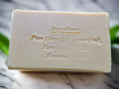 A beige bar of soap with the ingredients engraved on it, with a marble background and some green leaves.