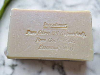 A beige bar of soap with the ingredients engraved on it with a marble background
