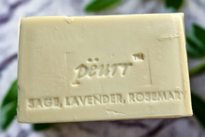 A bar of soap with 'PÈURR Sage, Lavender, Rosemary' engraved on it, against a floral patterned background.