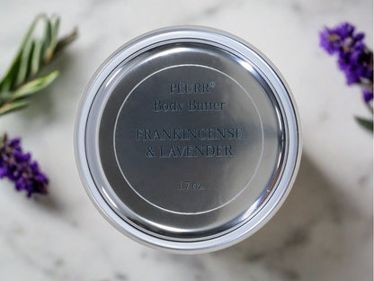 A jar of PëURR® Frankincense & Lavender Body Butter with lavender flowers around it.