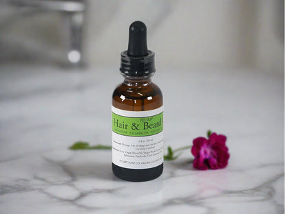 A bottle of PËURR Hair & Beard Oil with a dropper cap, labeled 'Green Label'. The bottle is placed on a marble surface with a flower in the background.