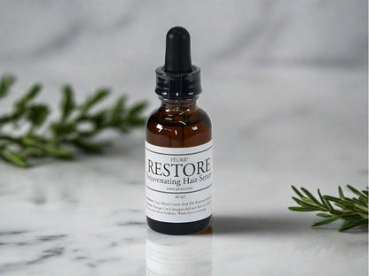 A bottle of PËURR® RESTORE Rejuvenating Hair Serum with a dropper, placed on a marble surface, flanked by green leaves on either side.